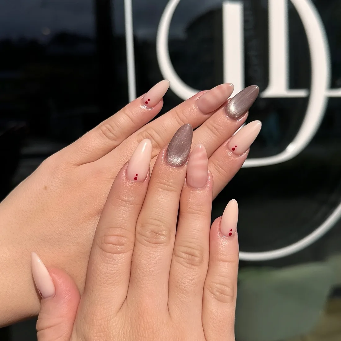 Gepflegte Nägel in Nude und Grau vor dem Schaufenster mit dem Della Logo